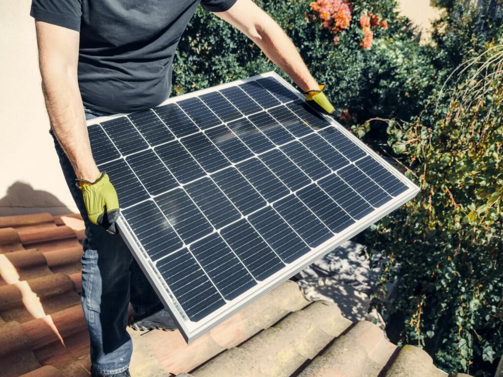 Home A worker in gloves installs a solar panel on a tiled rooftop, promoting renewable energy.